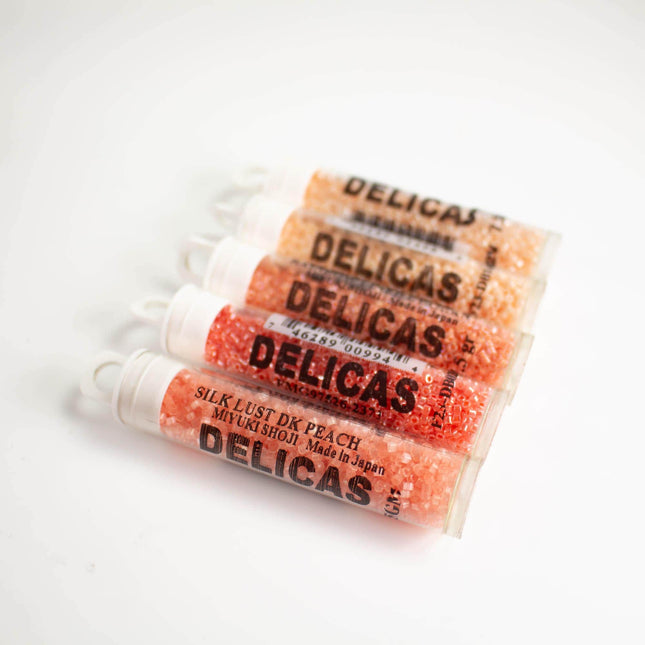 a row of four identical tubes of Delicas, each containing a small amount of a pink substance.