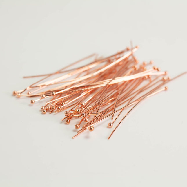 A pile of copper-colored metal pins or needles on a plain white background.