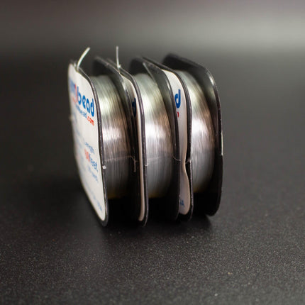 Three spools of silver thread are neatly arranged on a dark surface.