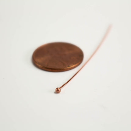 A copper wire with a small ball at the end is placed next to a penny on a white surface.
