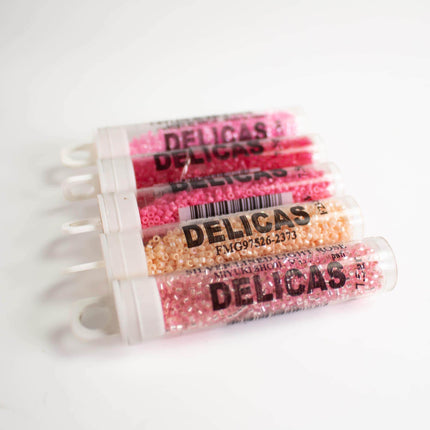 a collection of clear containers filled with pink and orange beads, labeled "DELICAS" in bold black text.