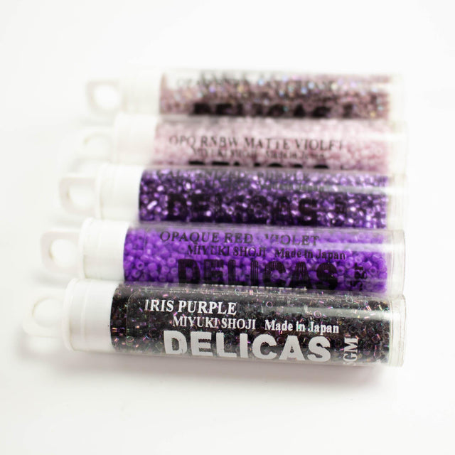 a collection of five clear plastic containers filled with various colored beads, including purple, black, and white beads.