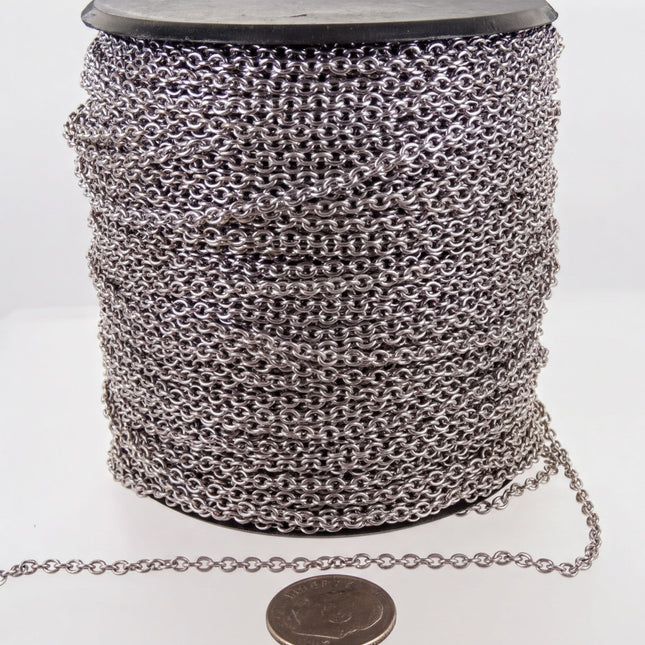 A spool of silver-colored metal chain is shown, with a small coin placed next to it on a white surface.