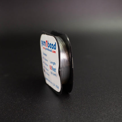 A spool of thread with the website "www.gembead.com" printed on it, sitting on a dark surface.