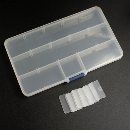 A clear plastic container with multiple compartments is placed on a dark surface, accompanied by several transparent plastic strips.