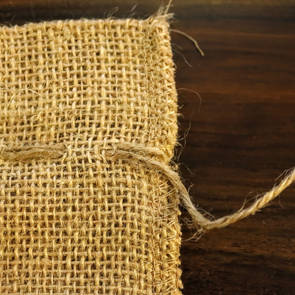 A close-up view of a piece of burlap fabric with a frayed edge, resting on a wooden surface.