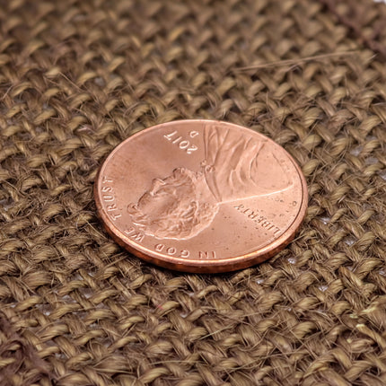 A close-up image of a United States penny resting on a woven surface.