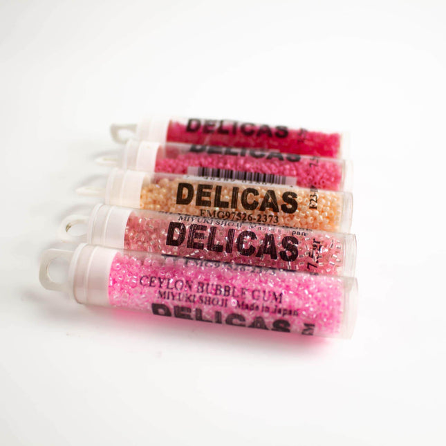 a collection of five cylindrical containers filled with a pink and orange substance, labeled as "Delicas" in black text.