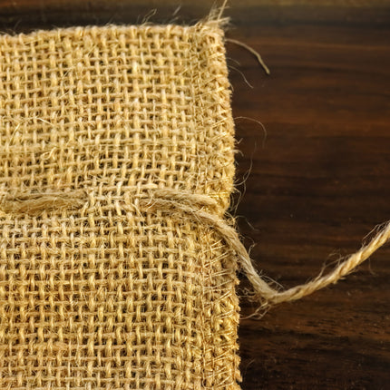 A close-up view of a piece of burlap fabric with a frayed edge, resting on a wooden surface.