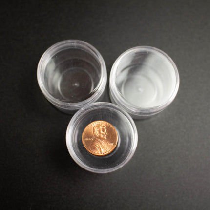 a clear plastic container with a penny inside, placed on a black surface.