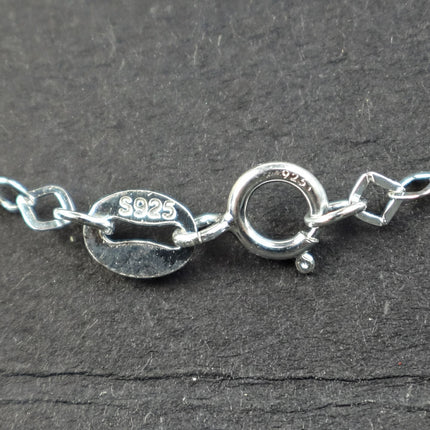 A close-up view of a silver necklace chain with a round clasp and a small oval-shaped tag with the number "9.25" printed on it.