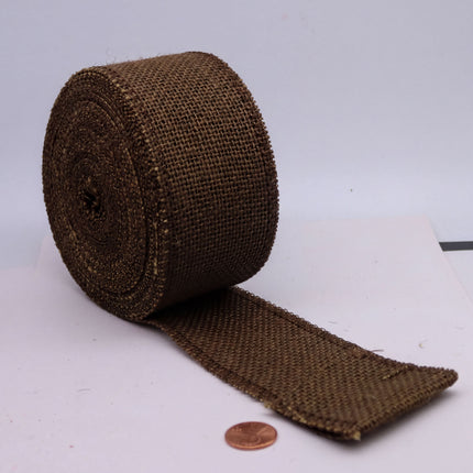 A roll of brown burlap material is placed on a white surface, with a penny lying next to it.