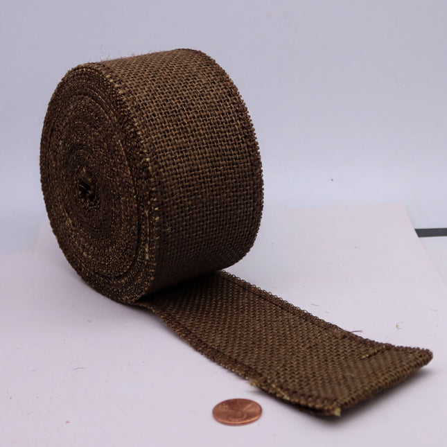 A roll of brown burlap material is placed on a white surface, with a penny lying next to it.