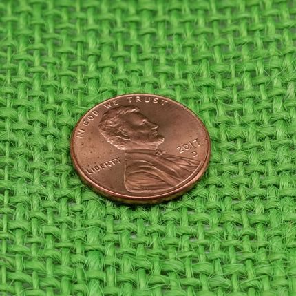 A close-up image of a United States penny resting on a green woven surface.