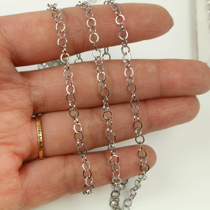 A hand holding a silver chain necklace with multiple silver rings.