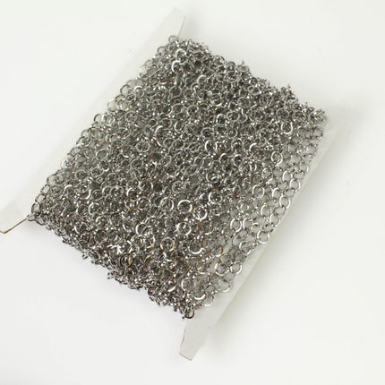 A spool of silver-colored metal chain with numerous small links, arranged in a crisscross pattern.