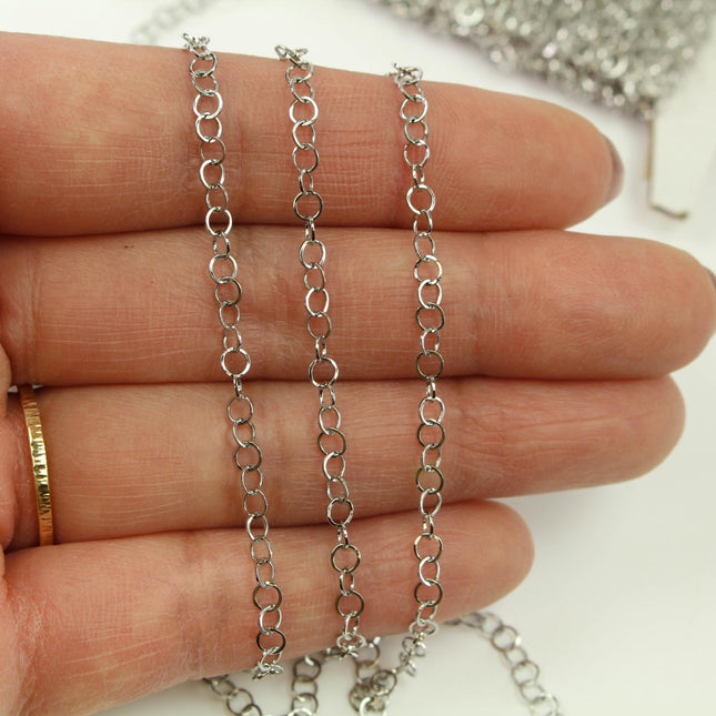 A close-up image of a person's hand holding a silver chain with multiple links, against a white background.