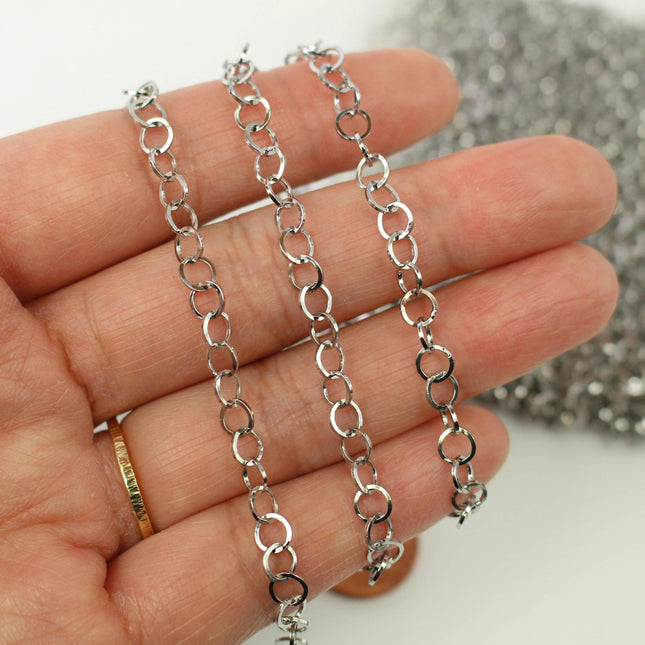 A hand holding a silver chain with multiple links, and a pile of silver wire or metal pieces in the background.