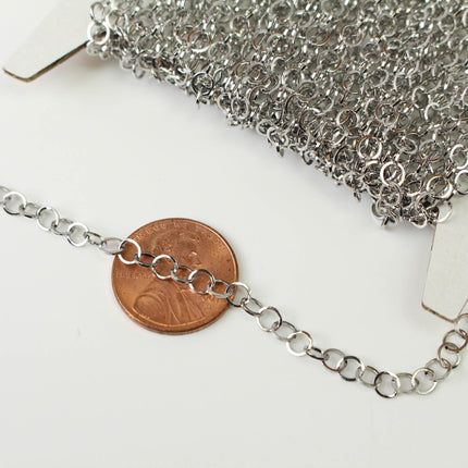 a close-up view of a silver chain with multiple circular links, placed next to a penny.
