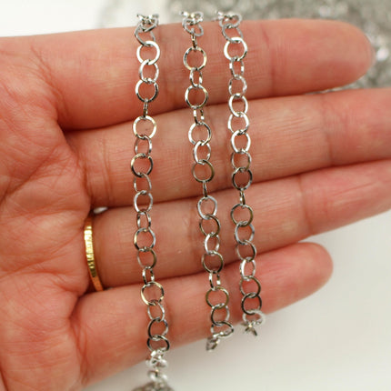 A hand holding a silver chain necklace with multiple silver rings.
