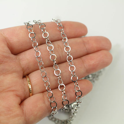 A hand holding a silver chain necklace with multiple silver rings.