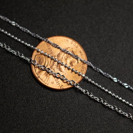 a close-up view of a small copper-colored coin placed on a black surface, with three silver chain necklaces arranged around it.