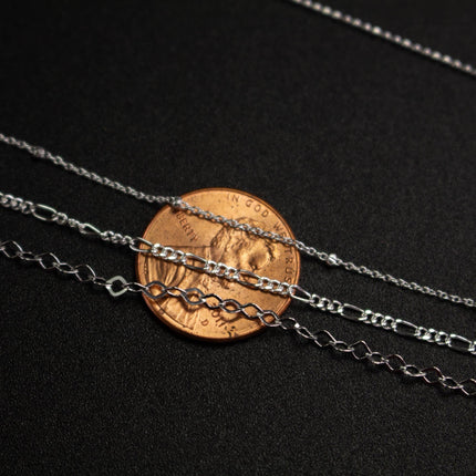 A close-up image of a collection of silver chain necklaces and a penny, with the penny placed on top of the necklaces.