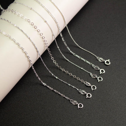 A collection of silver necklaces with various chain lengths and designs, arranged on a white surface.