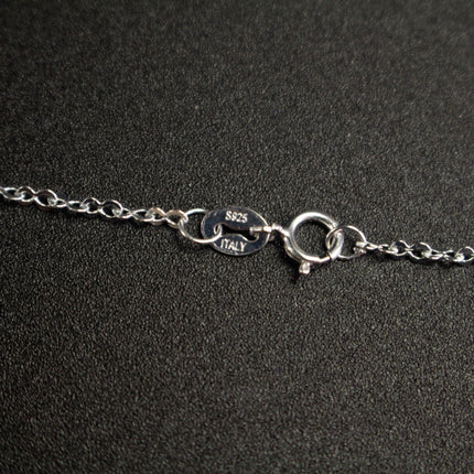 A close-up view of a silver necklace chain with a clasp and a small engraved label.
