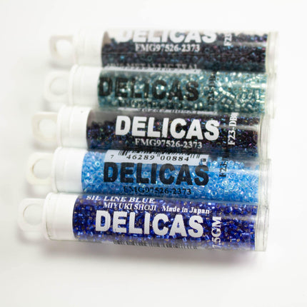 five cylindrical containers filled with blue and silver beads, each labeled with the brand name "DELICAS".