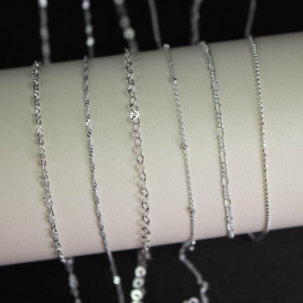 A collection of silver chain necklaces with various lengths and designs, displayed on a white surface.