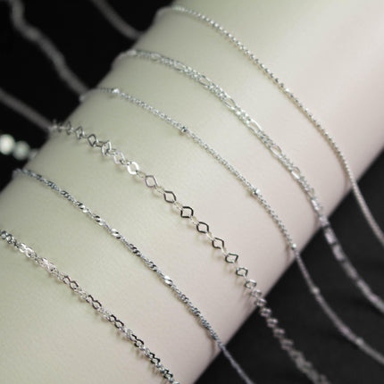 A close-up view of several silver-colored necklaces with various designs, displayed on a white surface.