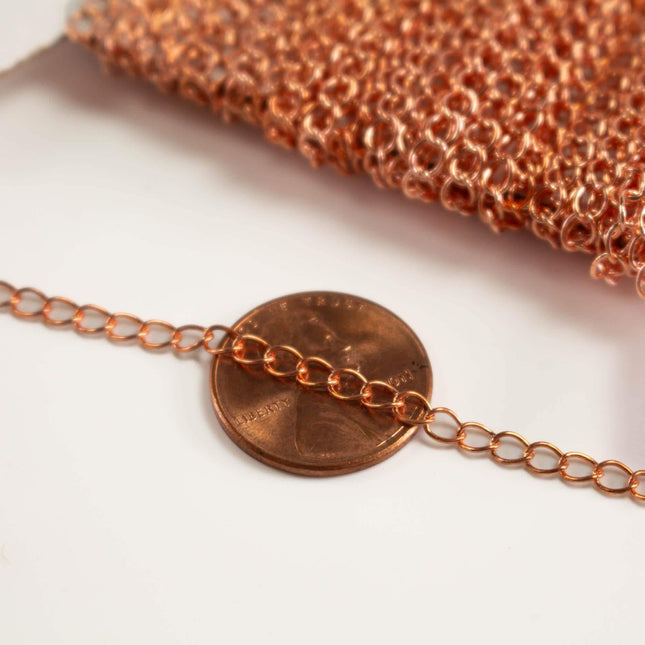 A close-up image of a copper-colored chain with a penny placed on top of it, against a white background.