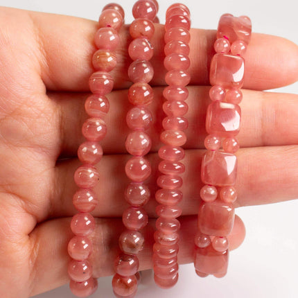 A hand holding several beaded bracelets in a row.