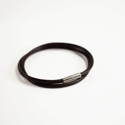A black leather bracelet with a silver clasp is shown against a white background.