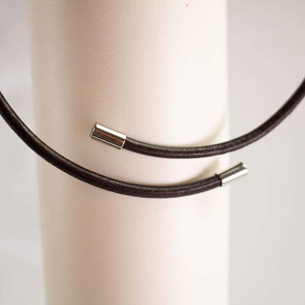 A close-up view of a black leather cord or bracelet with metal clasps, resting on a white surface.
