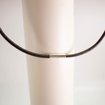 A black leather necklace with a silver clasp is shown against a white background.
