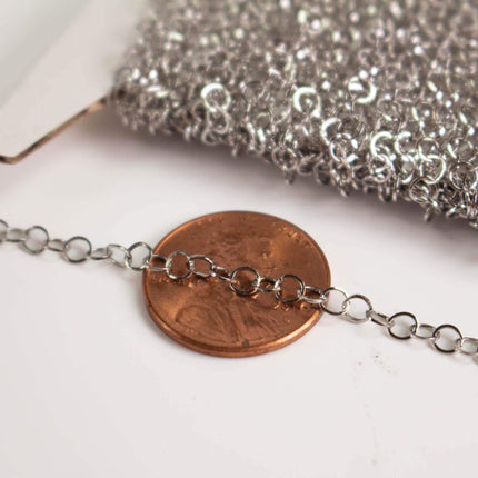 a close-up view of a copper-colored penny placed on a white surface, with a silver chain or wire chain extending from it.
