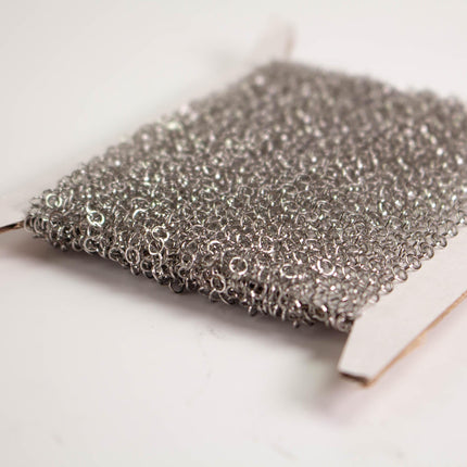 A close-up image of a piece of silver-colored metal mesh or chain against a white background.