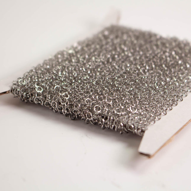 A close-up image of a piece of silver-colored metal mesh or chain against a white background.