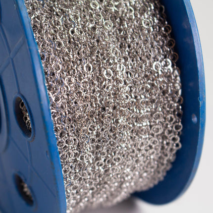A close-up view of a spool of silver chain with numerous small links, all of which are silver in color.