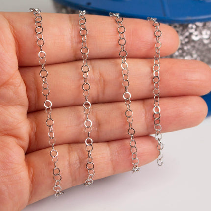 A hand holding multiple silver chain necklaces.