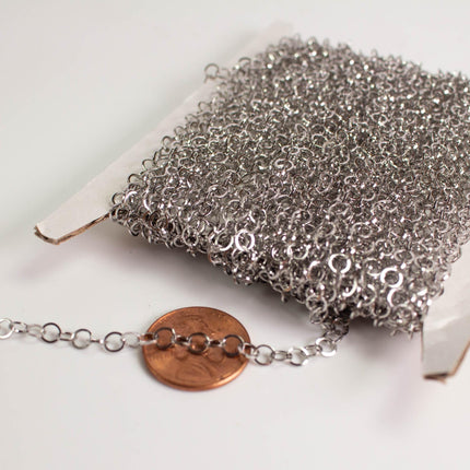 a close-up view of a silver chain with numerous small links, and a penny is placed next to it on a white surface.