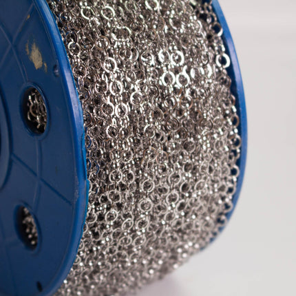 A close-up view of a spool of silver chain with multiple silver rings, against a white background.