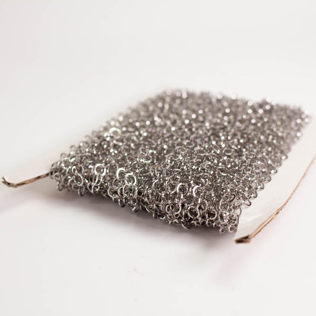 A close-up image of a piece of silver mesh or chain against a white background.