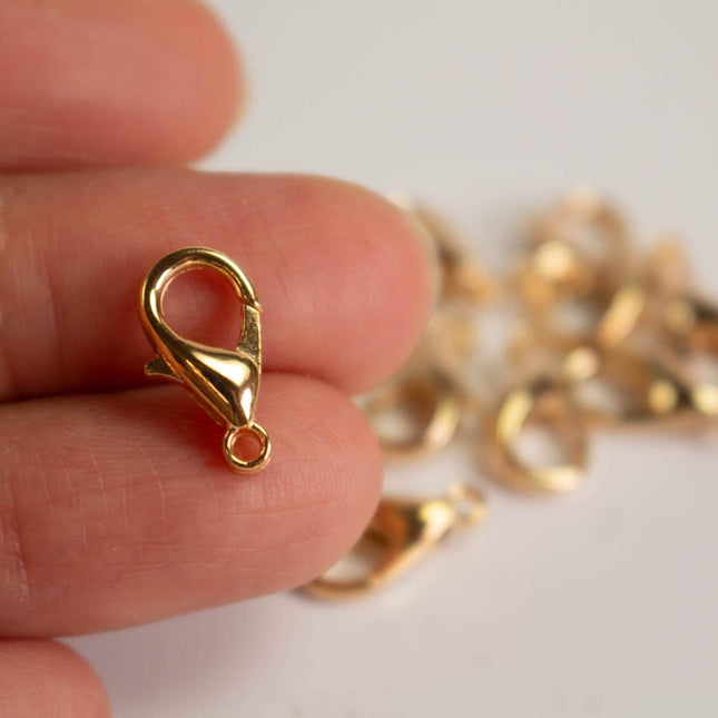 A hand holding a small gold-colored clasp on a white surface, with several gold-colored clasps in the background.