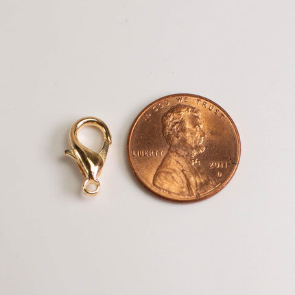A gold-colored metal clasp is placed next to a penny, which is a United States penny.