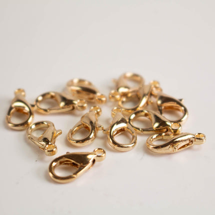 A group of shiny gold-colored metal clasp hooks or lobster hooks scattered on a white background.