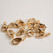 A group of shiny gold-colored metal clasp hooks or lobster hooks scattered on a white background.
