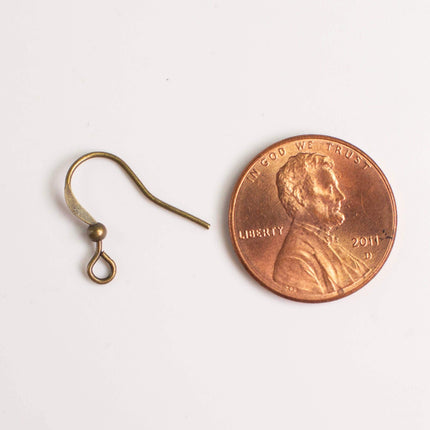 a small gold-colored earring hook next to a penny, which is a small copper-colored coin.